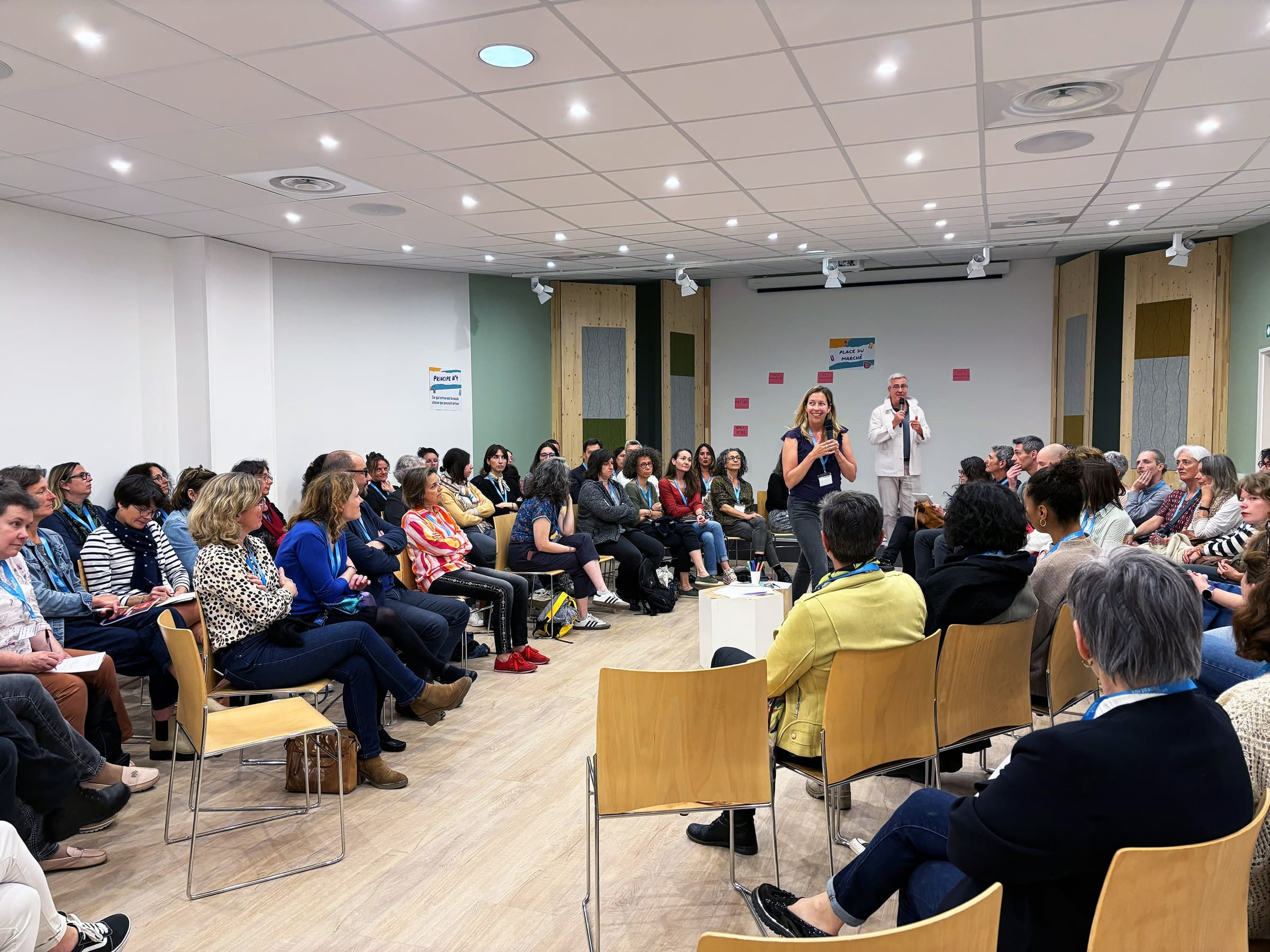 Un grand cercle de participants écoute Élise Delaunay, Jean-Luc Guillou debout en retrait