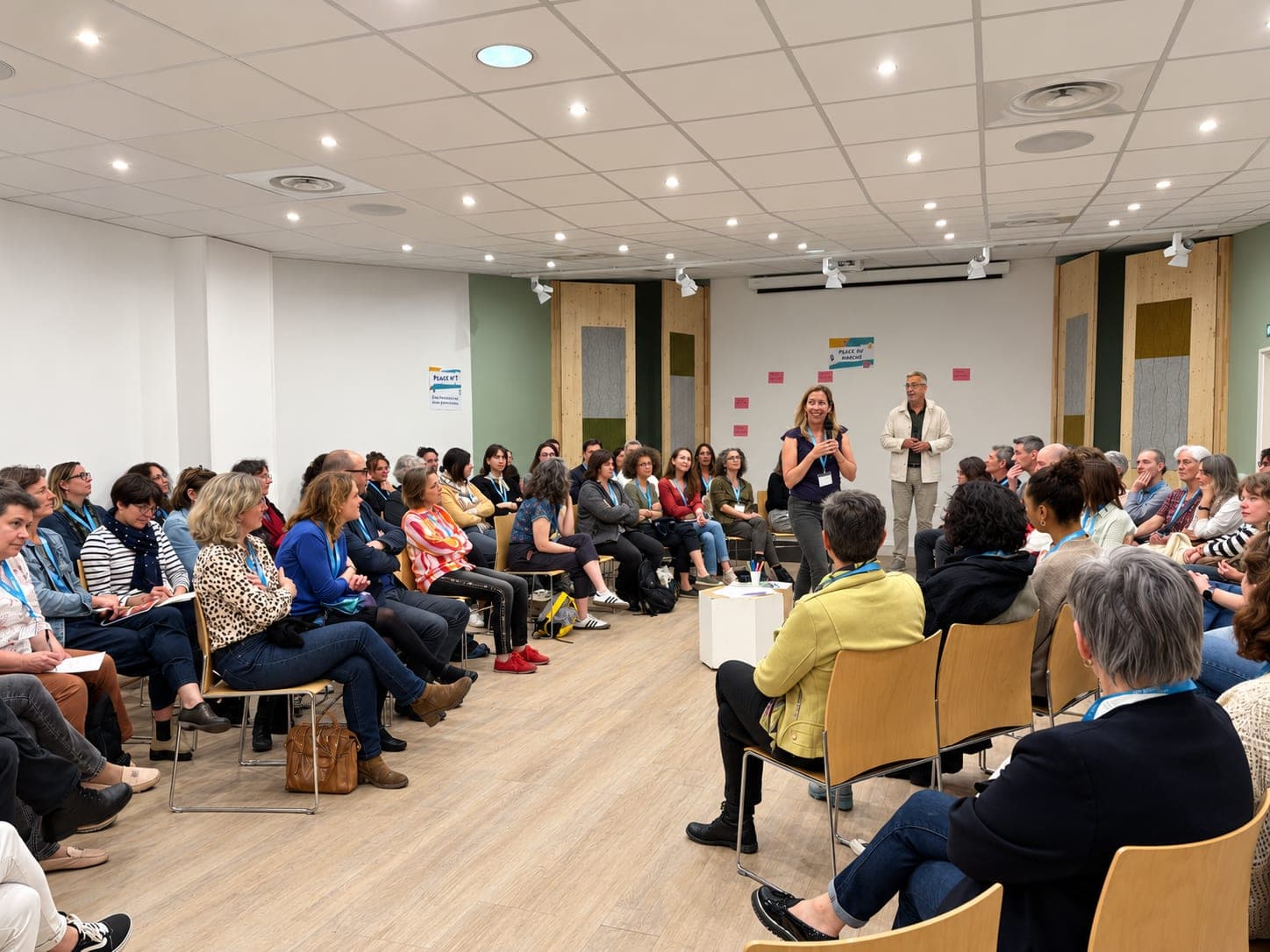 Un grand cercle de participants écoute Élise Delaunay, Jean-Luc Guillou debout en retrait